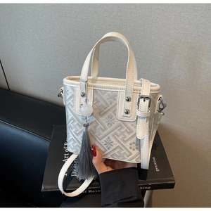 Détail du sac seau crème avec broderie géométrique et décoration de pompon gris