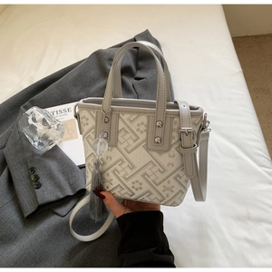 Détail du sac seau géométrique gris avec pompon et breloque perlée dans une scène lifestyle