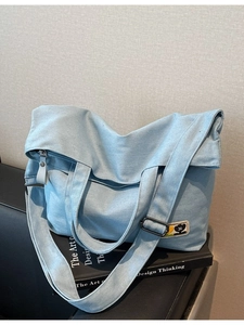 Light blue canvas tote bag with floral embroidery and adjustable strap on a book