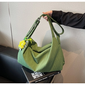 Detail of green pleated shoulder bag featuring yellow floral pendant and acrylic chain