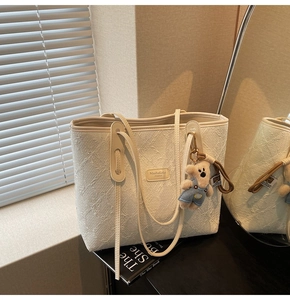 Gros plan d'un sac cabas blanc texturé avec logo en cuir et breloque ours en peluche