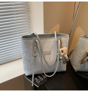 Détail du sac cabas bleu clair à fleurs gaufrées avec breloque ours sur bureau noir