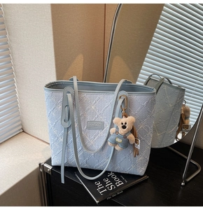 Détail du sac cabas bleu clair brodé de fleurs avec un porte-clés ours en peluche
