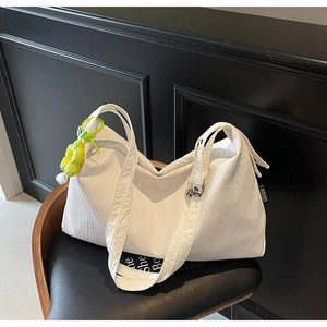 Detailed view of white pleated tote bag with a vibrant green flower pendant detail