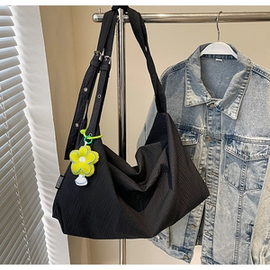 Detail of black pleated tote bag with wide shoulder strap and yellow flower charm