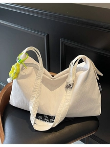 Minimalist white large capacity tote bag with pleated texture and floral pendant on dark seat
