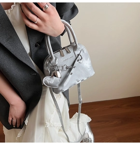 Sac à main argenté avec pendentif coeur porté sur un blazer gris chic