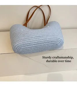 Detail of light blue woven straw bag featuring durable stitching and brown leather strap