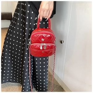 Close-up of red quilted patent leather handbag with silver chain strap and floral buckle