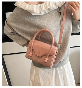 Détail du sac à main en cuir rose avec texture tressée et logo porté par un mannequin