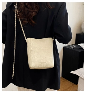 Close-up of beige lychee texture bucket bag with chain strap on dark blazer