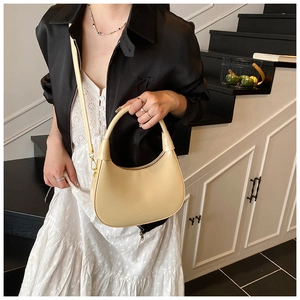 Chic cream crescent shoulder bag with adjustable strap worn by model in modern interior