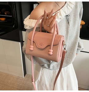 Détail du sac à main rose en cuir avec texture tressée et finitions dorées chic