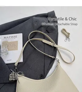Detail of creamy white pebble grain shoulder bag with wide adjustable strap and metal charm