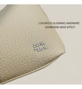 Detailed close-up of beige lychee grain leather texture and silver metal logo on handbag