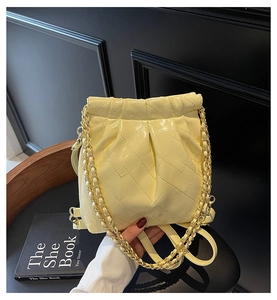 Detail of light yellow quilted bucket bag with gold chain strap on a vintage background