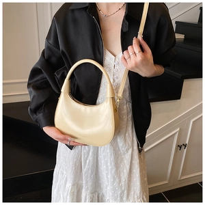 Dettaglio di una borsa a tracolla a mezzaluna crema in pelle liscia con zip metallica