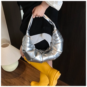 Detail shot of a silver metallic pleated croissant bag held by a fashion model indoors