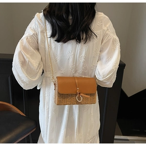 Straw crossbody bag with brown leather flap and gold ring detail on model's back