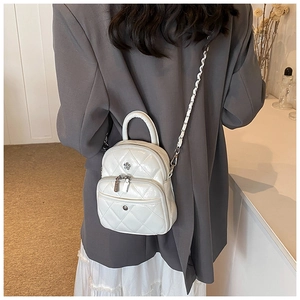 Detail view of white quilted mini backpack with silver flower charm on gray blazer