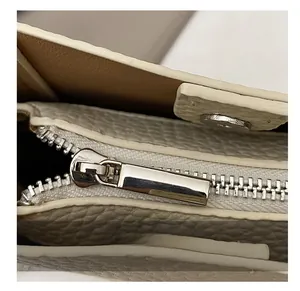 Detail shot of smooth silver zipper and magnetic clasp on cream lychee grain leather bag