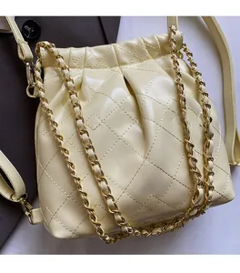 Detail view of cream quilted bucket bag with gold chain strap and drawstring closure