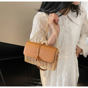 Detail of a straw box bag featuring a caramel leather flap and golden chain strap