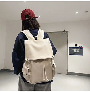 Rear view of a person wearing a cream faux leather travel backpack with drawstring flap