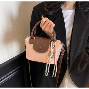 Detail of pink and brown crossbody bag with woven pendant held by a model