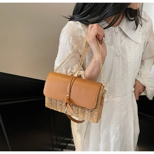 Detail of woven straw bag with brown leather flap and gold chain strap on lace dress