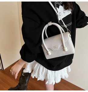Détail du sac crème avec texture tissée et logo métallique Pan Tor sur le rabat