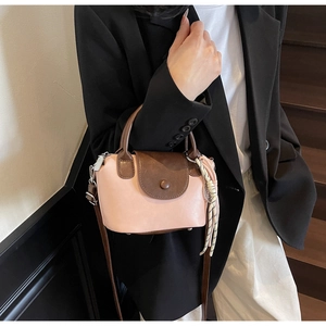Detail view of pink leather handbag with contrast brown flap and woven rope charm