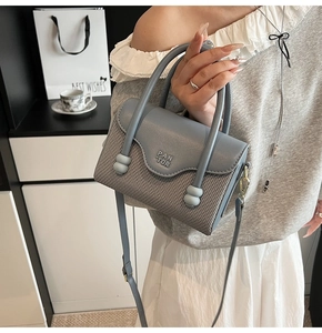 Gros plan du sac à main bleu-gris avec détail de boule dorée et logo PAN TOR gravé