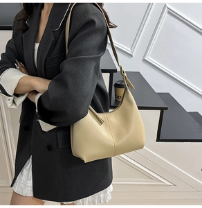 Detail view of cream hobo shoulder bag with adjustable strap worn by model in gray suit
