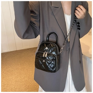 Quilted black leather mini bag detail shown on model with silver floral logo and chain strap