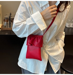 Gros plan du sac bandoulière rouge avec texture litchi et détails de volants sur chemise