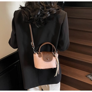 Close-up of pink and brown crossbody bag with woven pendant and adjustable strap