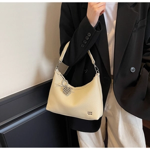 Detail of cream hobo bag in lychee leather with silver heart charm on black blazer