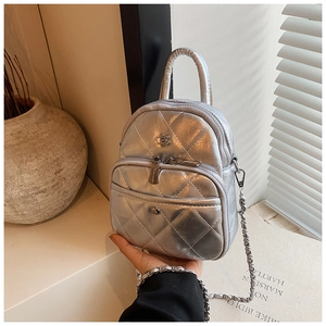 Detail of silver quilted crossbody bag with flower accent and chain strap held by hand