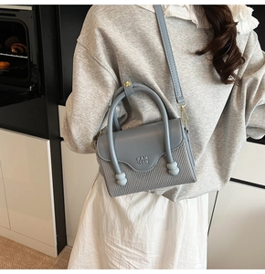 Détail du sac bandoulière bleu gris avec surpiqûres en cuir et accents de texture tissée