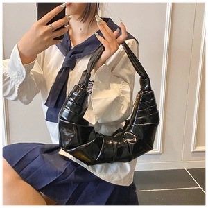 Detailed view of black pleated dumpling bag with glossy finish and half-moon shape