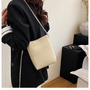 Close-up of cream leather bucket bag showing lychee grain texture and chain strap detail