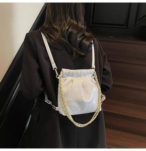 Detail view of white quilted bucket bag with gold chain strap on a dark blazer