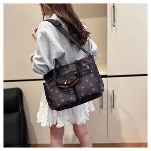 Détail du sac cabas noir à imprimé cerise porté par un mannequin avec bandoulière réglable