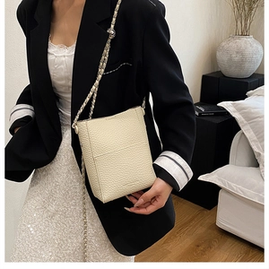 Detail of cream white pebbled leather bucket bag with braided chain shoulder strap