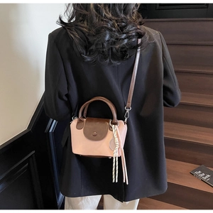 Detail of a pink and brown crossbody bag with woven tassel charm shown on a model