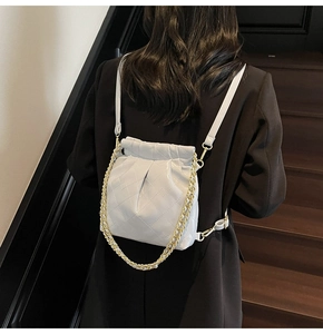 Detail of light grey quilted bucket bag featuring gold chain and soft pleated texture