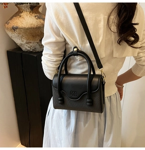 Détail du sac bandoulière noir mêlant cuir et texture tissée avec logo embossé sur le rabat