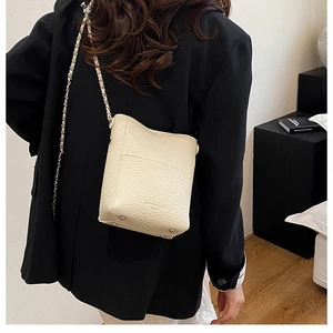 Detail view of cream white lychee pattern bucket bag with golden chain strap on a model