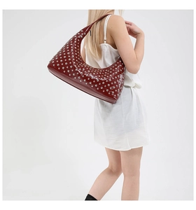 Detail of dark red rivet studded hobo shoulder bag worn by model in white dress